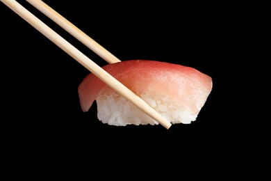 Photo of Chopsticks with delicious nigiri sushi on black background, closeup