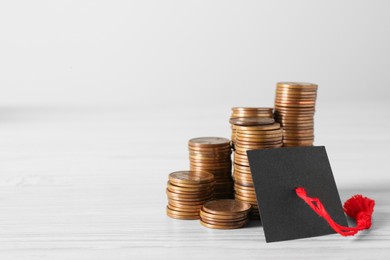 Photo of Scholarship concept. Graduation cap and stacked coins on white wooden table, space for text