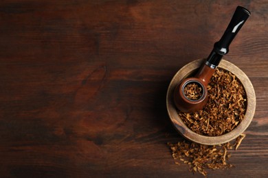Smoking pipe and bowl of dry tobacco on wooden table, top view. Space for text