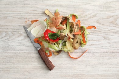 Photo of Peels of fresh vegetables and knife on white wooden table, flat lay