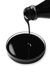 Pouring black crude oil into Petri dish on white background