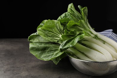 Photo of Fresh green pak choy cabbages with water drops in sieve on grey table, closeup