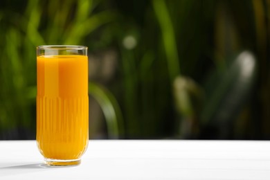 Photo of Glass with tasty carrot juice on white table outdoors. Space for text