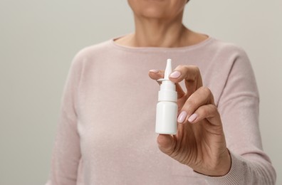 Photo of Closeup of woman holding nasal spray against light grey background, focus on bottle. Space for text