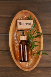 Photo of Card with word Retreat, green branch, cosmetic bottle and sea salt on wooden table, top view