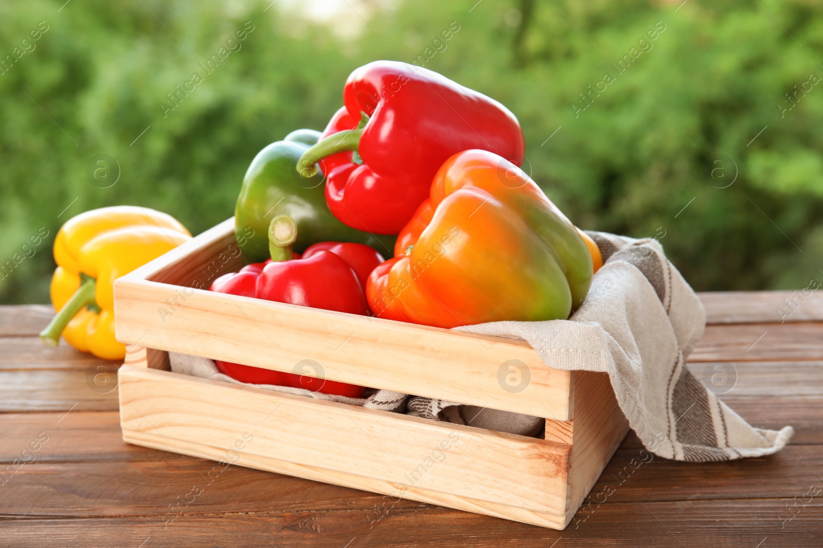 Photo of Crate with ripe paprika peppers on table against blurred background