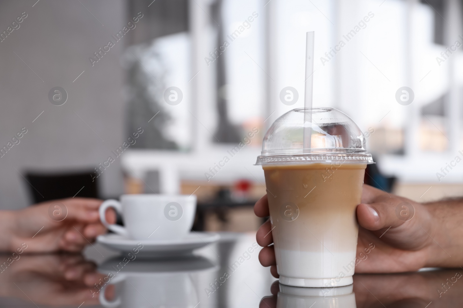 Photo of Man with plastic takeaway cup of delicious iced coffee at table in outdoor cafe, closeup. Space for text