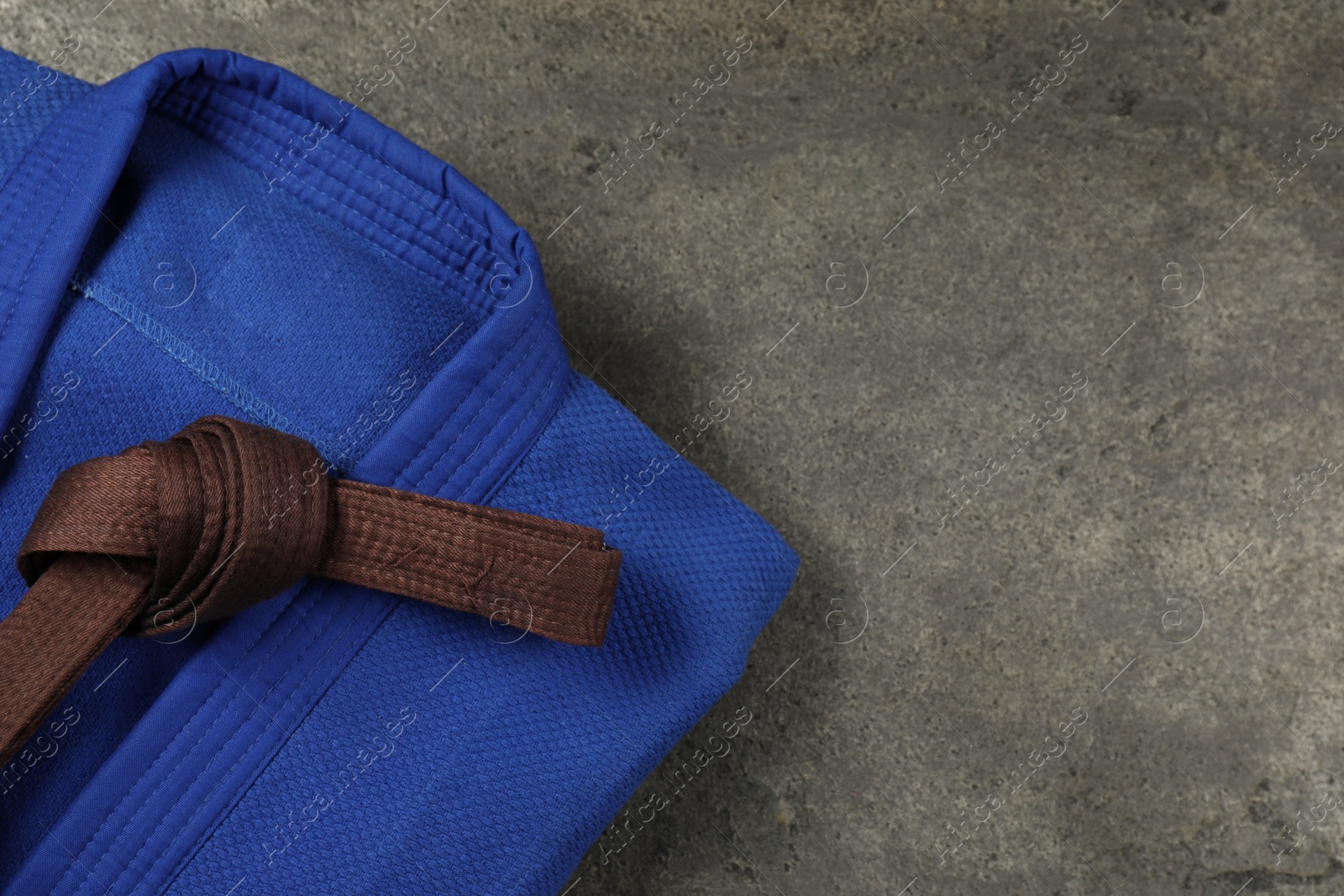 Photo of Brown karate belt and blue kimono on gray textured background, top view. Space for text