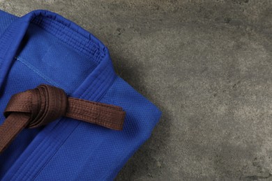 Photo of Brown karate belt and blue kimono on gray textured background, top view. Space for text