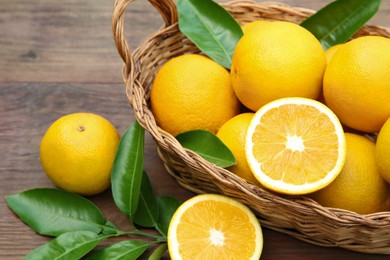 Wicker basket, ripe juicy oranges and green leaves on wooden table, closeup