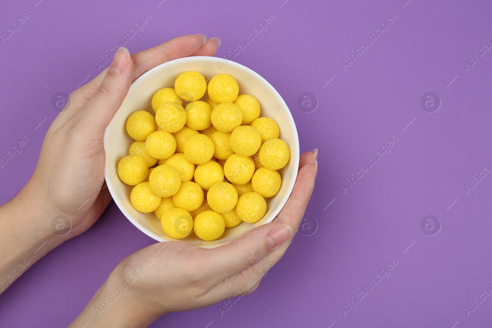 Photo of Woman holding bowl of lemon drops on purple background, top view