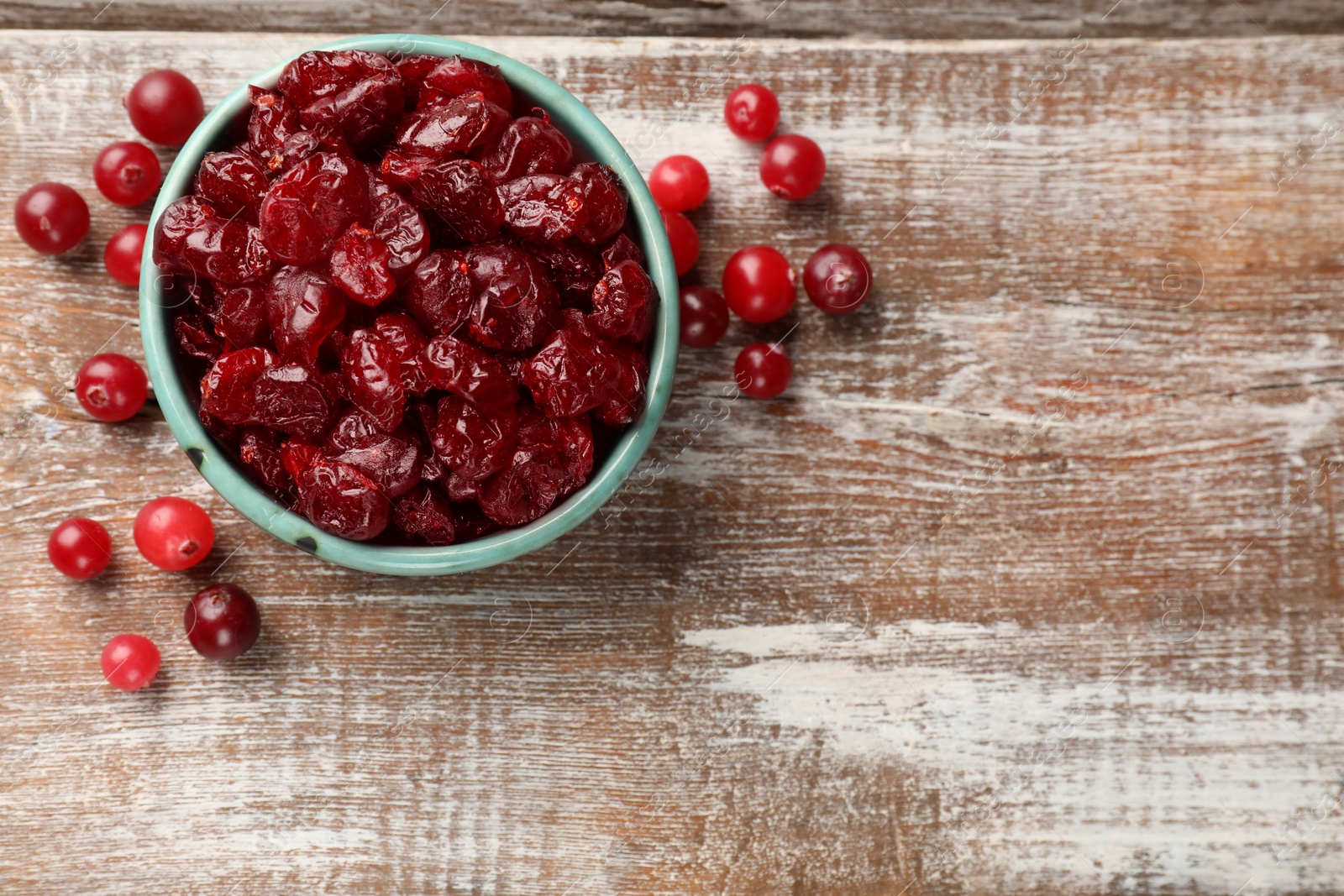 Photo of Tasty dried cranberries in bowl and fresh ones on rustic wooden table, top view. Space for text