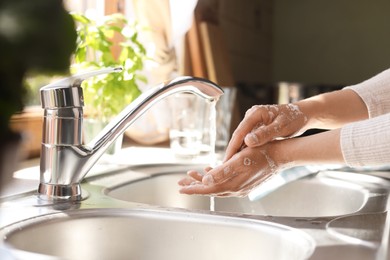 Photo of Woman washing hands in kitchen, closeup view