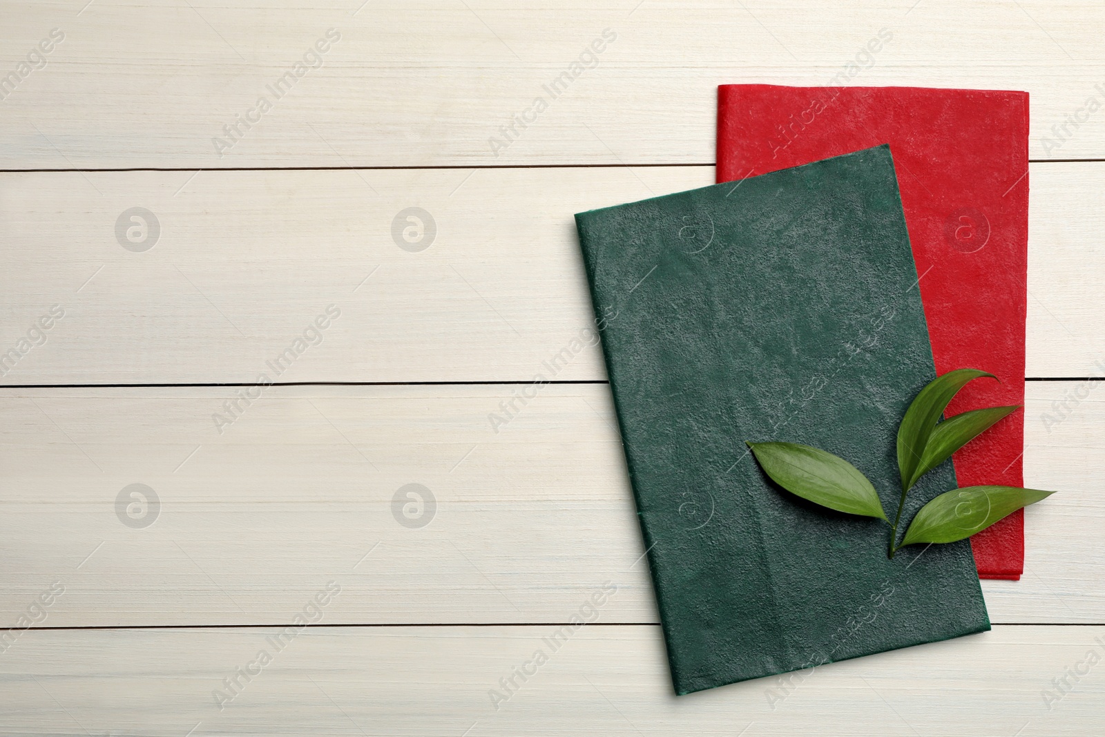 Photo of Colorful beeswax food wraps and fresh leaves on white wooden table, top view. Space for text