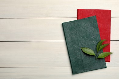 Photo of Colorful beeswax food wraps and fresh leaves on white wooden table, top view. Space for text