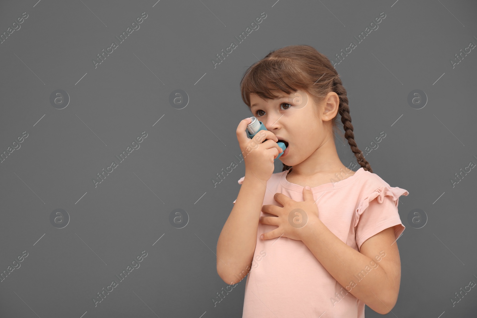 Photo of Little girl using asthma inhaler on grey background