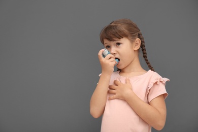 Photo of Little girl using asthma inhaler on grey background