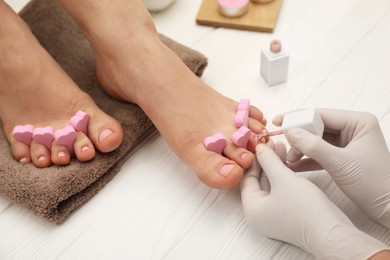 Professional pedicurist painting client`s toenails with polish in beauty salon, closeup