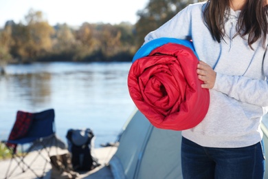 Young woman with sleeping bag near camping tent outdoors, closeup. Space for text