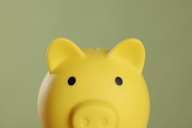 Yellow piggy bank on olive background, closeup. Space for text