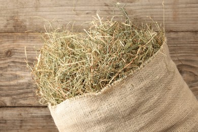 Photo of Burlap sack with dry herb on wooden table, top view