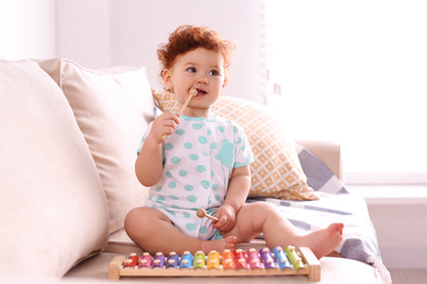 Photo of Cute little child playing with xylophone on sofa at home