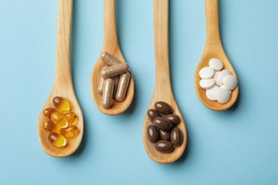 Photo of Wooden spoons with different dietary supplements on light blue background, flat lay