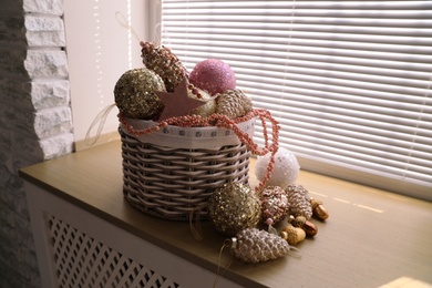 Basket with beautiful Christmas tree baubles on window sill indoors