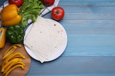 Photo of Delicious folded Armenian lavash and fresh vegetables on light blue wooden table, flat lay. Space for text
