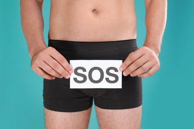 Man holding SOS sign on turquoise background, closeup. Urology problems