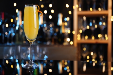 Photo of Mimosa cocktail with garnish on bar counter against blurred lights, space for text