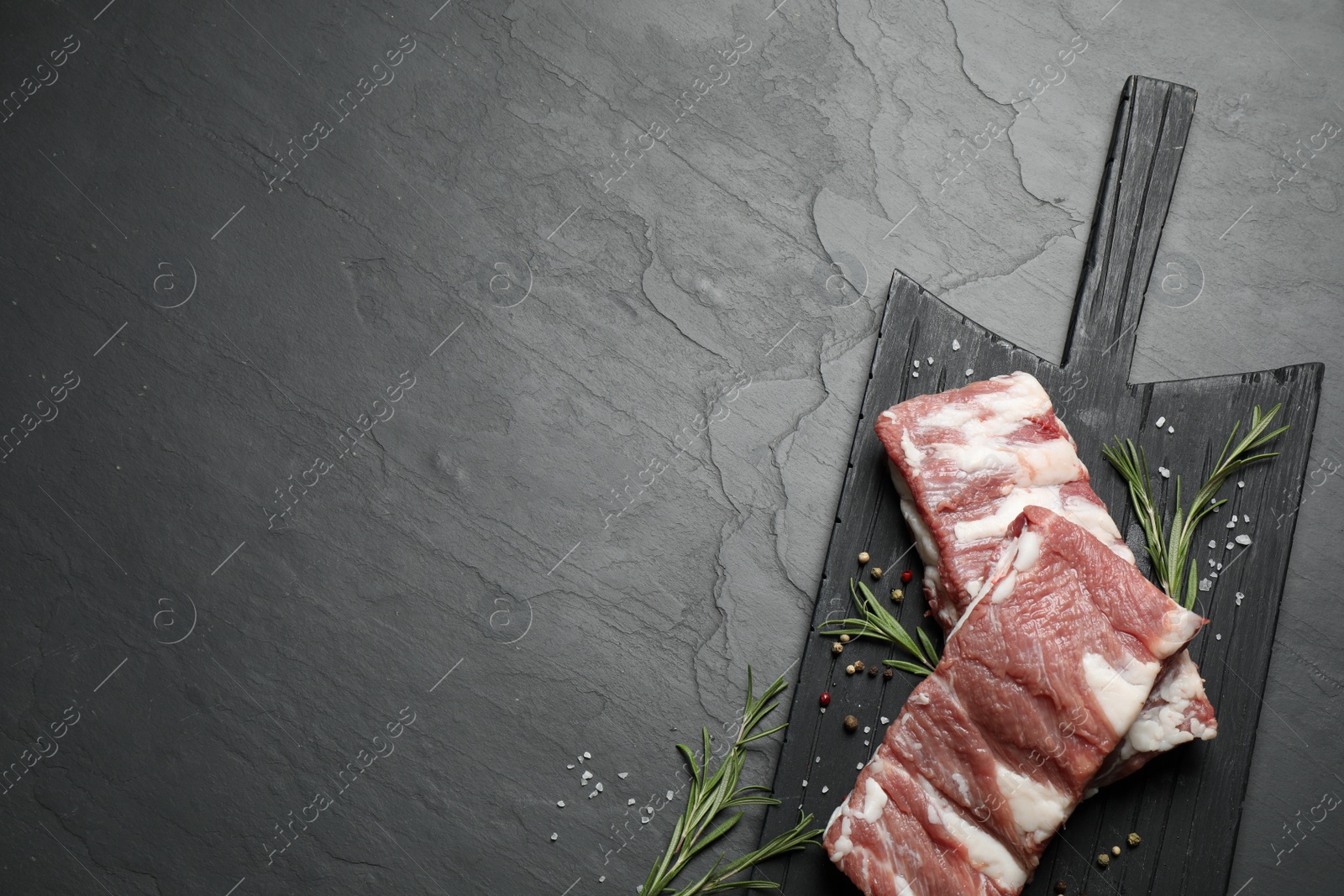 Photo of Raw ribs with rosemary and spices on black table, top view. Space for text