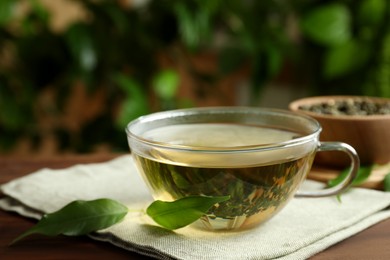 Photo of Fresh green tea in glass cup and leaves on table
