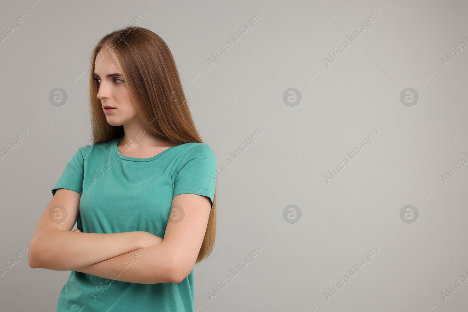 Photo of Resentful woman with crossed arms on grey background, space for text