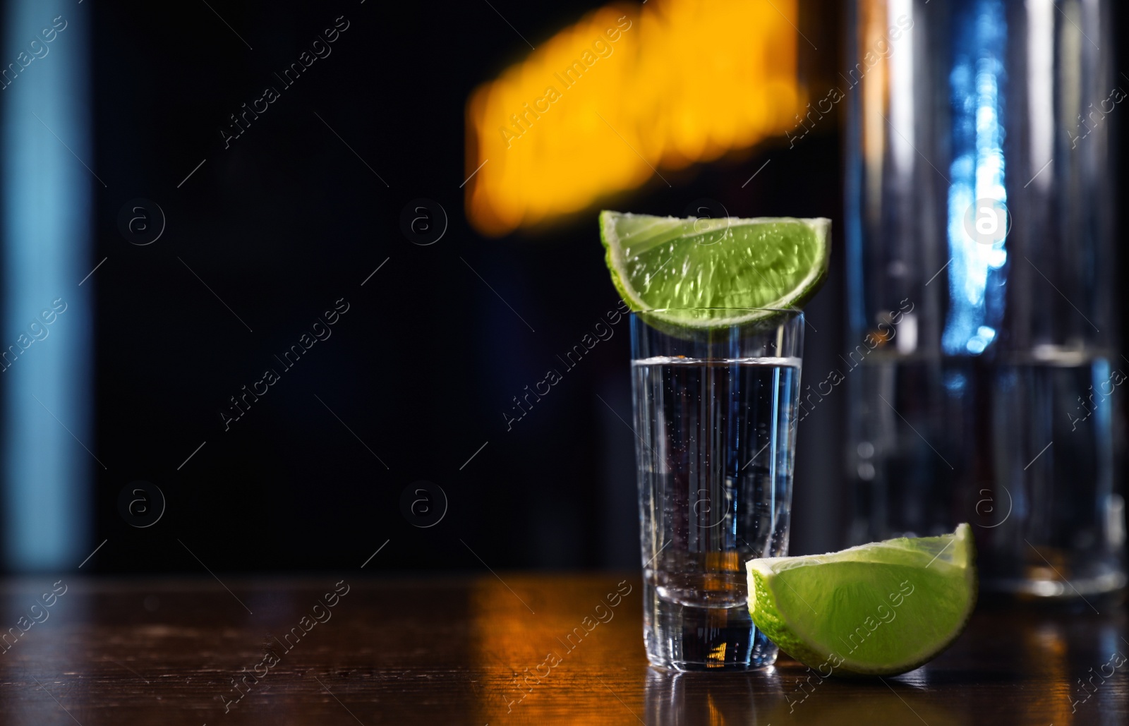 Photo of Mexican Tequila shot with lime slices on wooden bar counter. Space for text