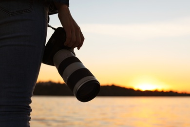 Photo of Female photographer with professional camera on riverside at sunset