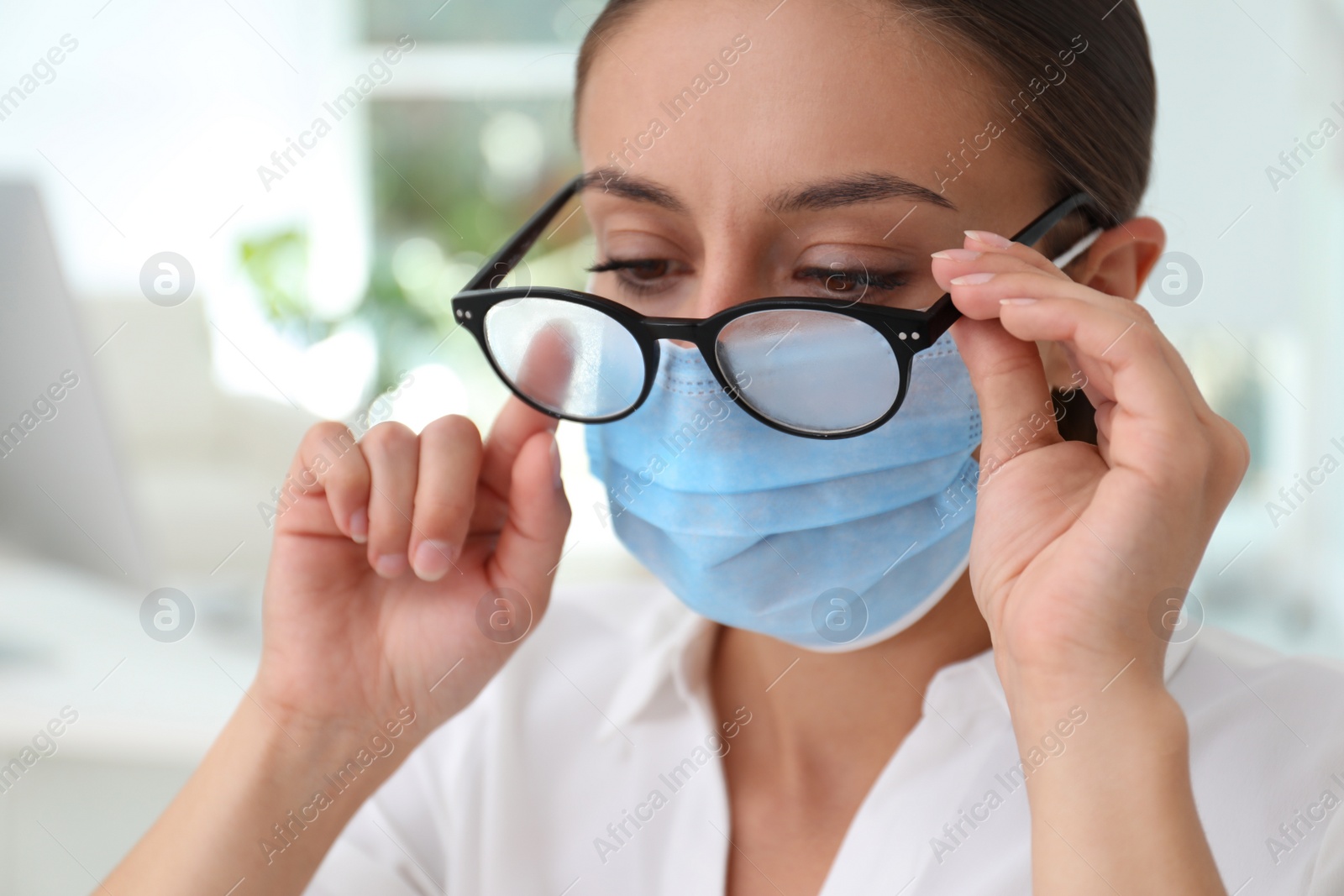 Photo of Woman wiping foggy glasses caused by wearing medical mask indoors, closeup