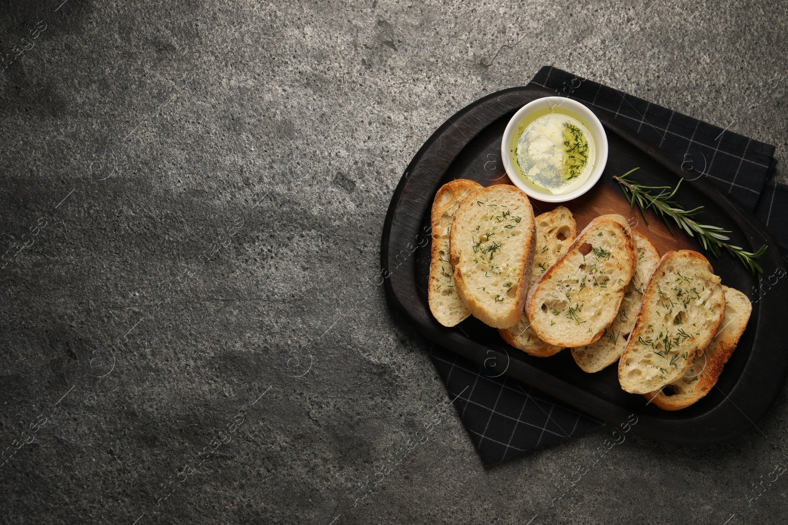 Photo of Tasty baguette with garlic and dill served on grey textured table, top view. Space for text