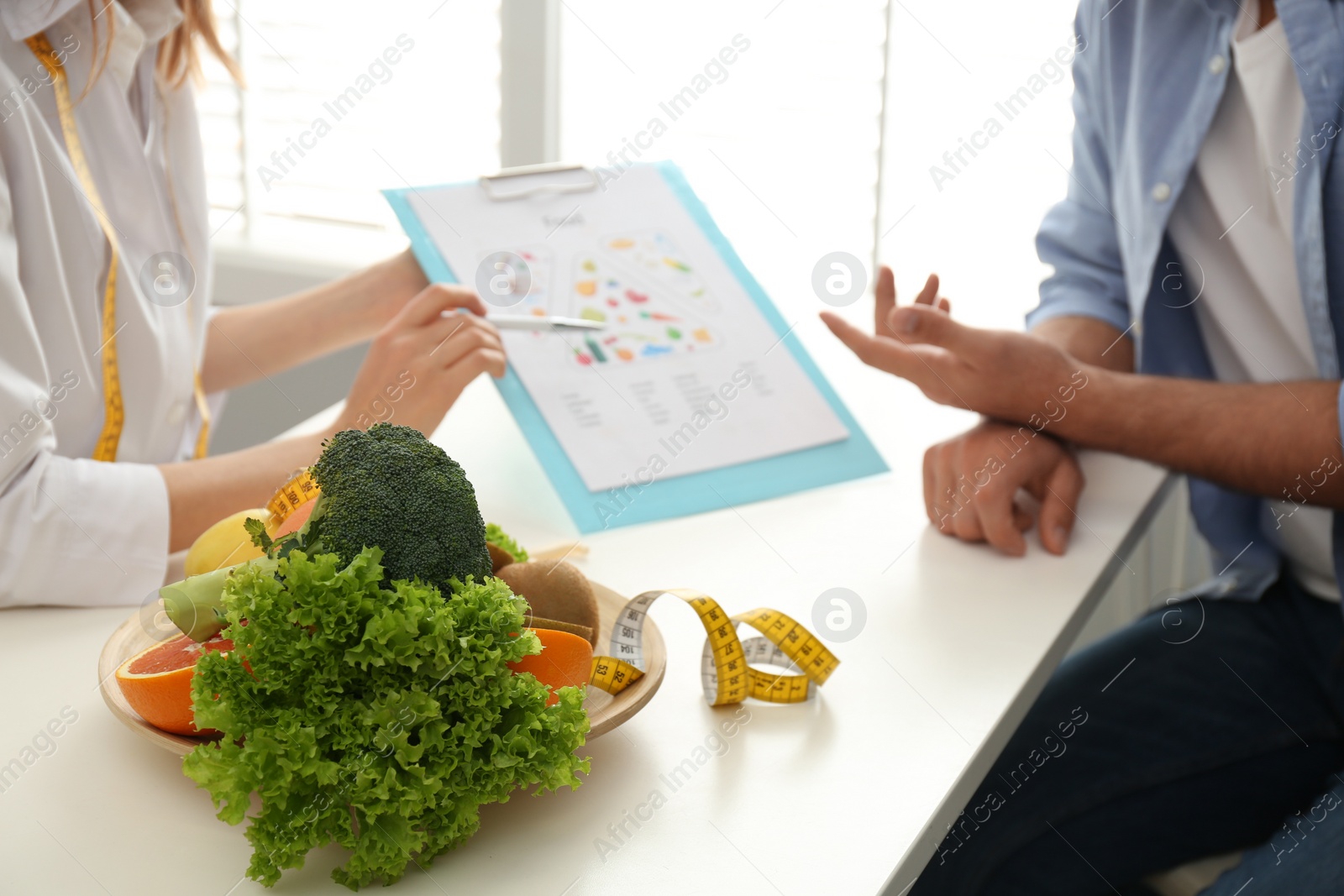 Photo of Young nutritionist consulting patient at table in clinic, closeup