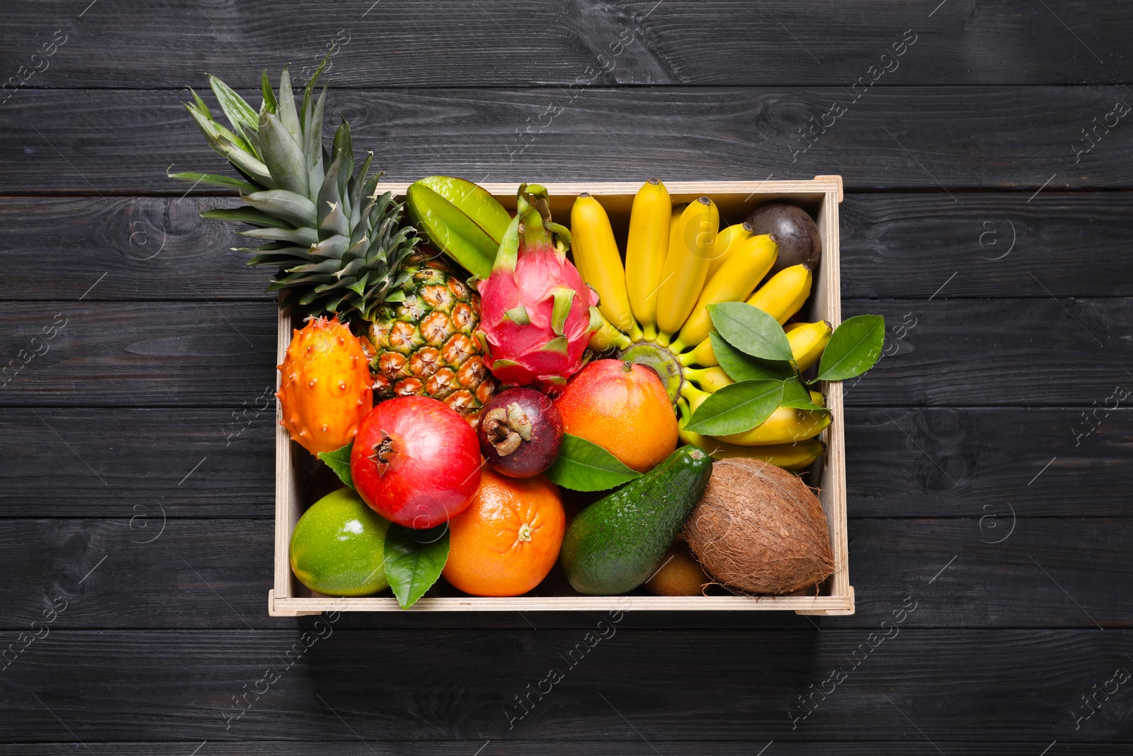 Photo of Crate with different exotic fruits on black wooden table, top view