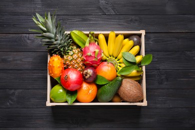 Crate with different exotic fruits on black wooden table, top view
