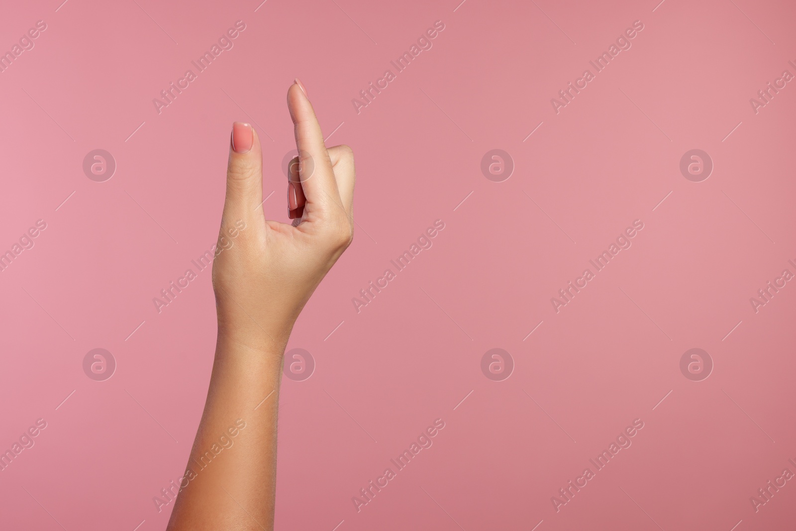 Photo of Woman holding something in fingers on pink background, closeup. Space for text