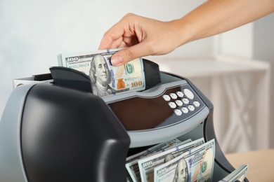 Photo of Woman putting money into counting machine indoors, closeup