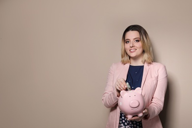 Photo of Businesswoman putting money into piggy bank on color background. Space for text