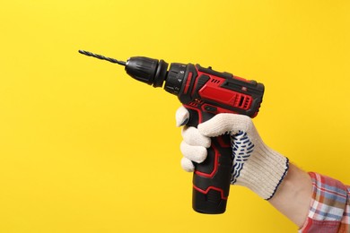 Photo of Handyman holding electric screwdriver on yellow background, closeup