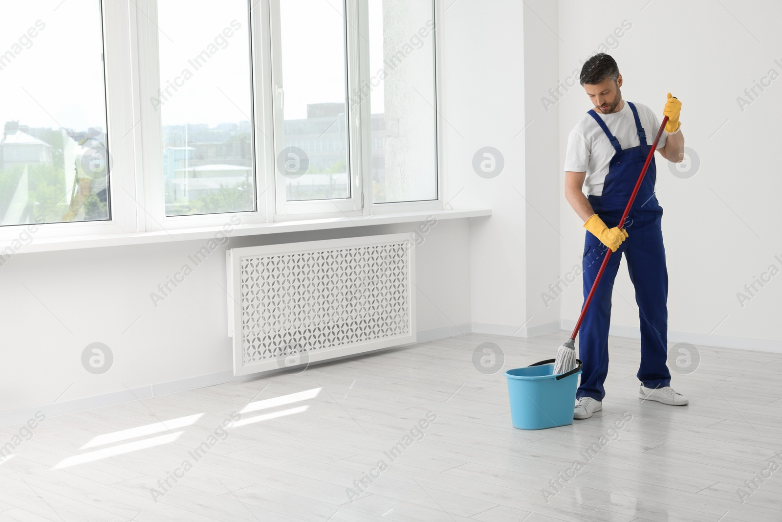 Photo of Man in uniform putting mop into bucket indoors. Space for text