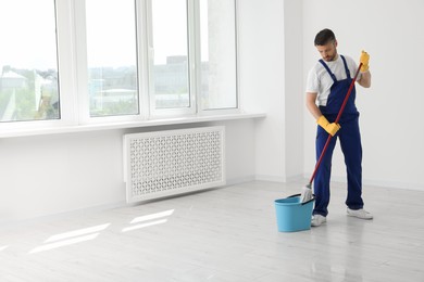 Photo of Man in uniform putting mop into bucket indoors. Space for text