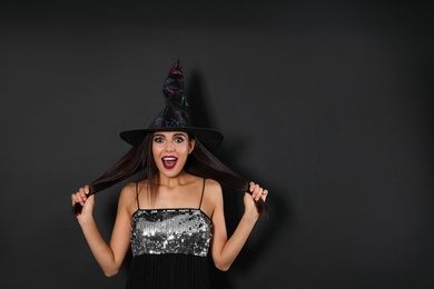 Photo of Excited woman wearing witch costume for Halloween party on black background, space for text