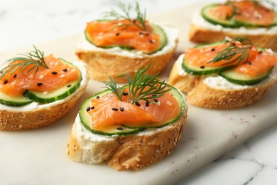 Photo of Tasty canapes with salmon, cucumber and cream cheese on white marble table, closeup