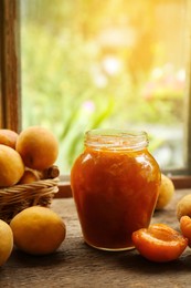 Jar of delicious jam and fresh ripe apricots on wooden table indoors. Fruit preserve